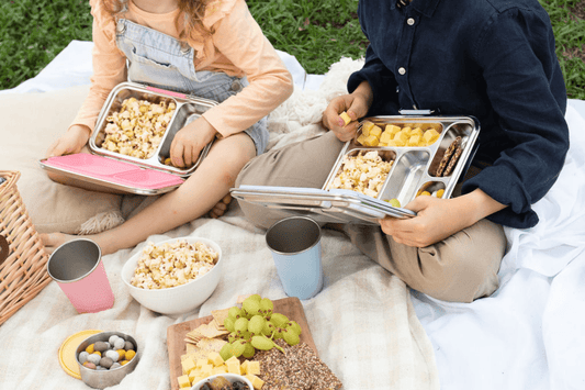 children sitting on a picnic blanket with bento lunchboxes filled with popcorn cheese and crackers