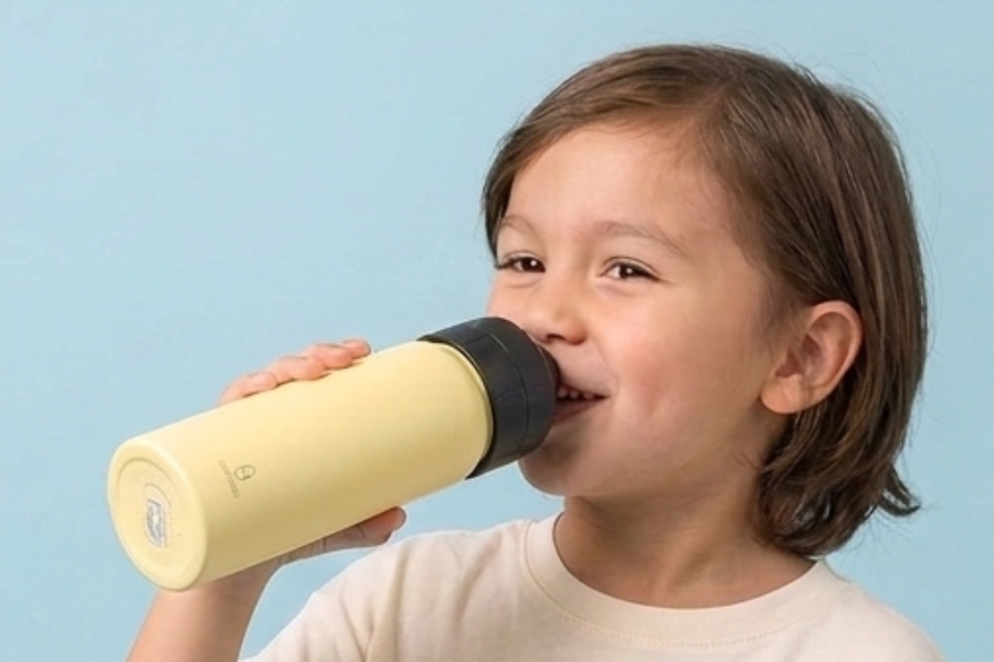 Young boy in front of a blue background drinking from a yellow EcoCocoon bottle