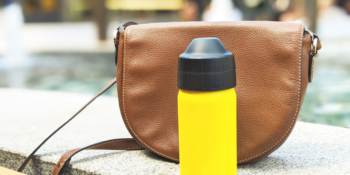 yellow stainless steel drink bottle in front of brown leather bag