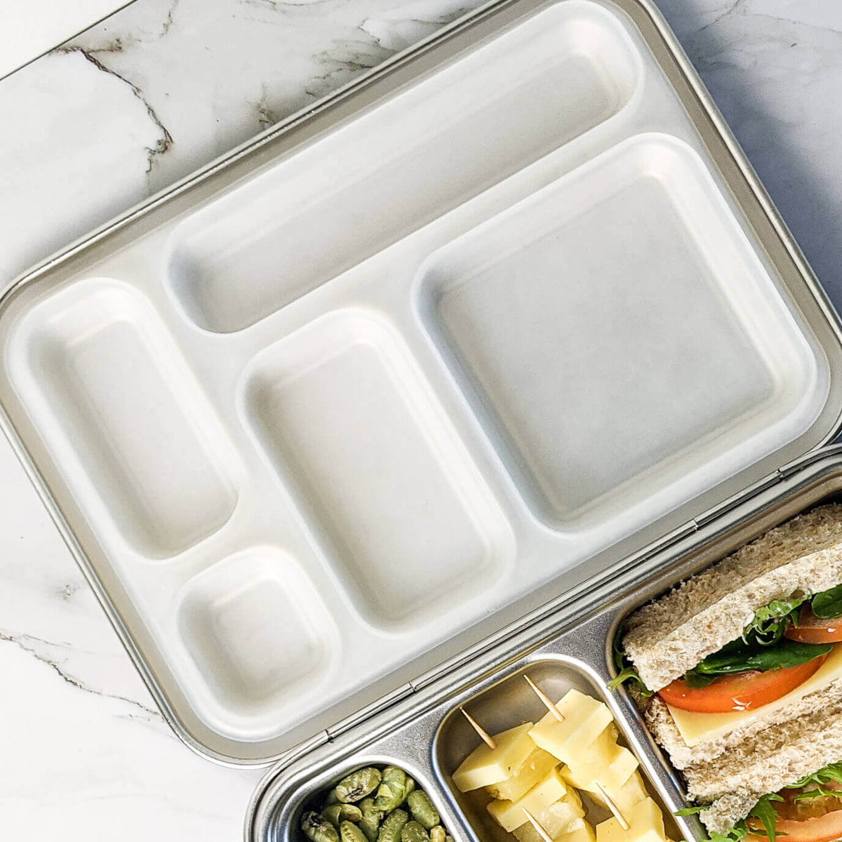 White replacement silicone seal in a five-compartment bento lid beside a packed sandwich